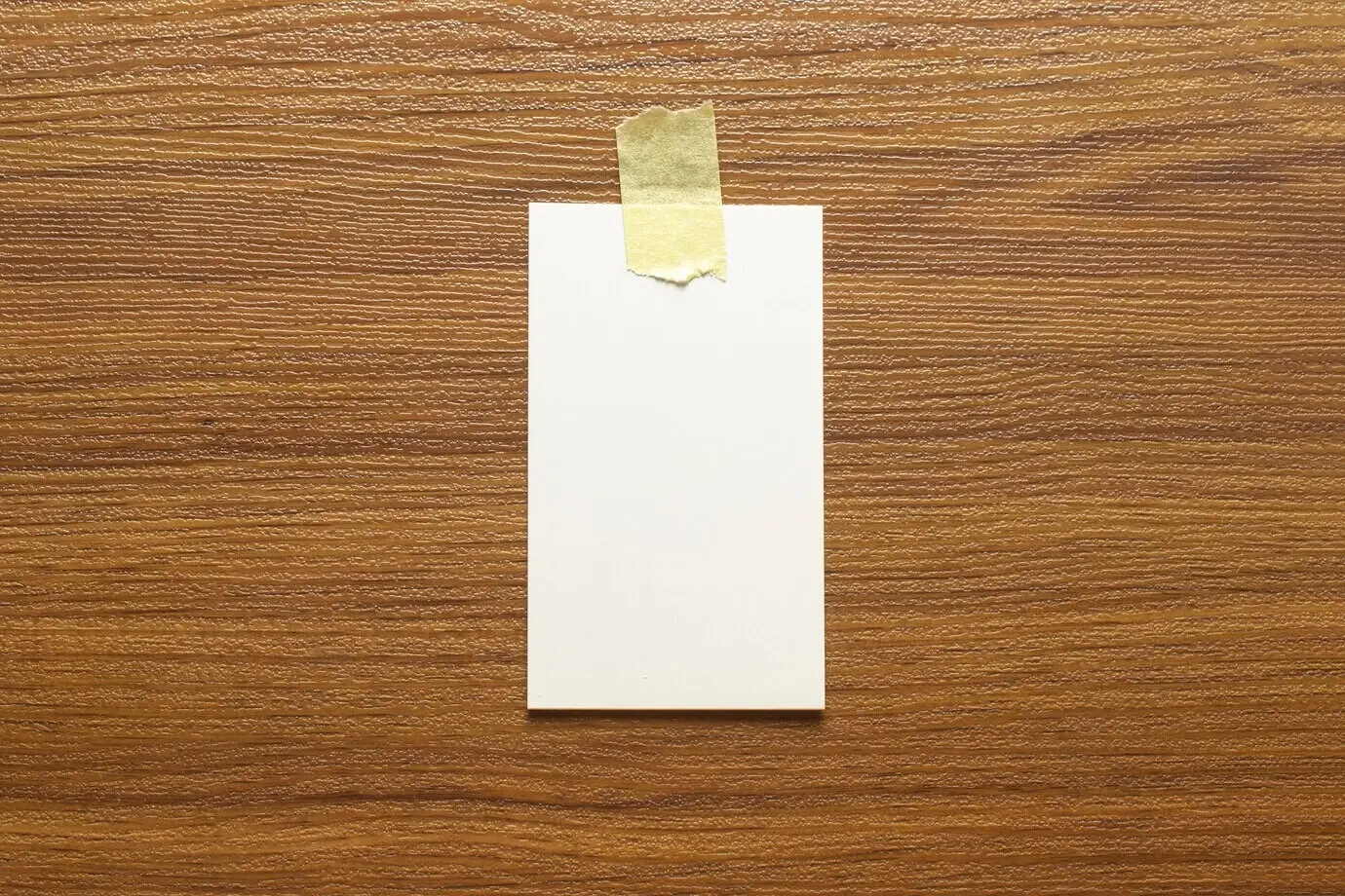 Чистые визитные карточки размером 3,5 × 2 дюйма, приклеенные жёлтой клейкой лентой на деревянной поверхности, со свободным пространством.
